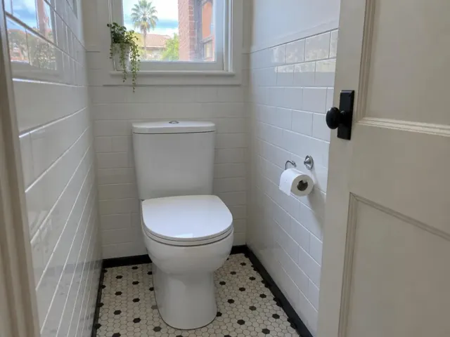 Clean white toilet in a small tiled bathroom with patterned floor and open door in Bondi